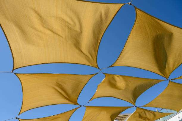 Geometric pattern of tan shade sails providing overhead sun protection against a blue sky.