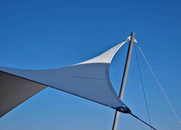 White triangular shade sail corner secured to a metal pole against a clear blue sky.