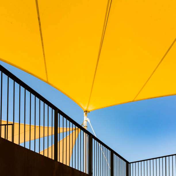 Bright yellow shade sail providing overhead sun protection, with a railing against blue sky.